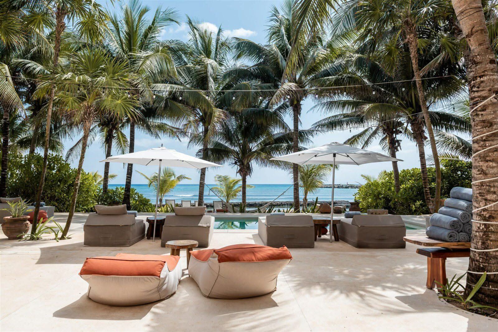 Tropical resort patio with lounge chairs, umbrellas, palm trees, and ocean view