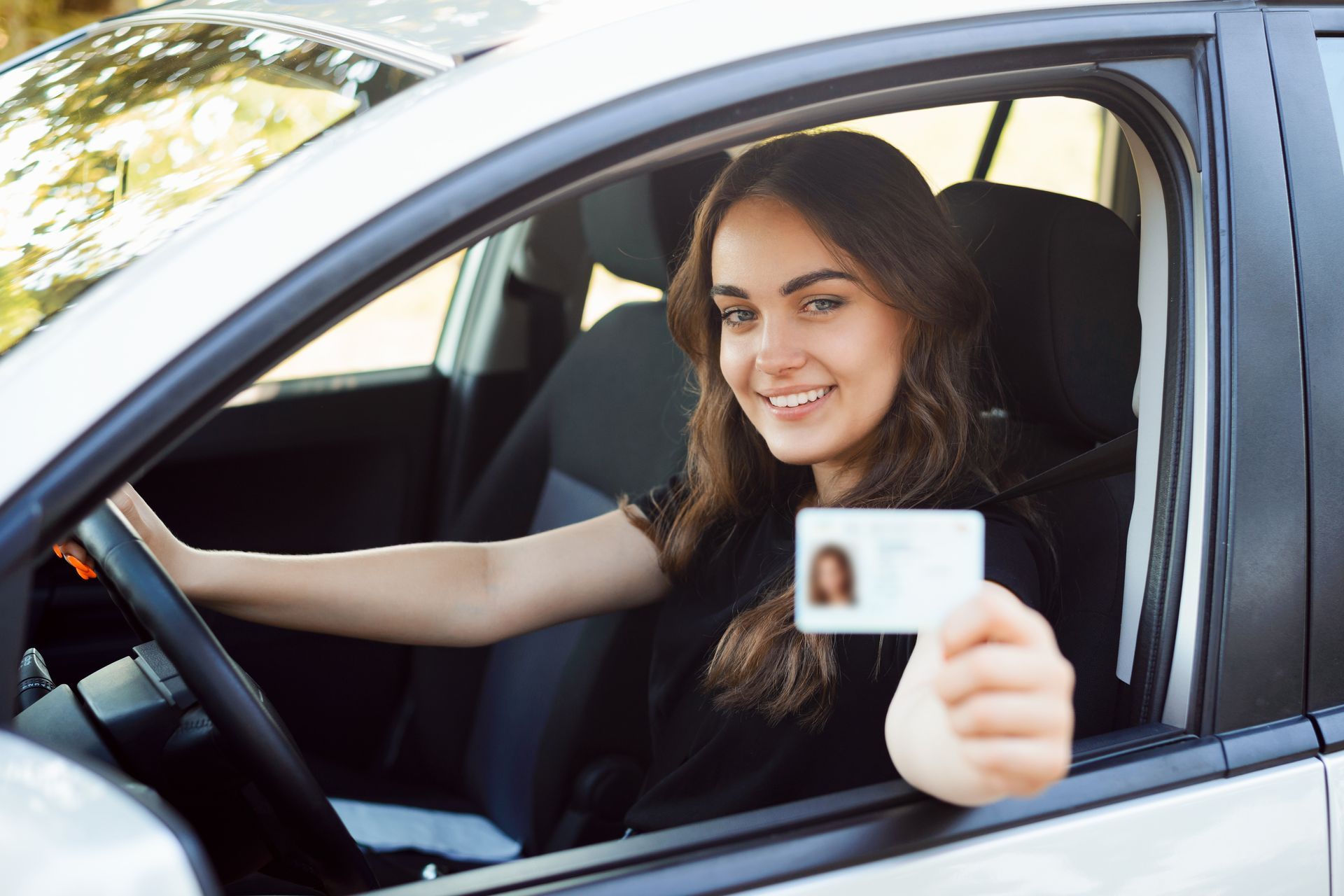 Femme souriante dans une voiture, tenant son permis de conduire.