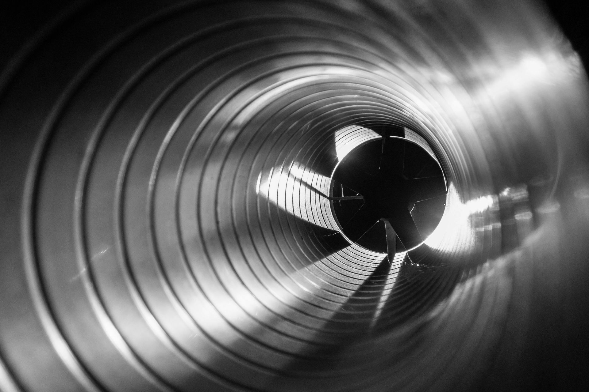 Vue intérieure d'un tube métallique ondulé, centre sombre, extrémité lumineuse.