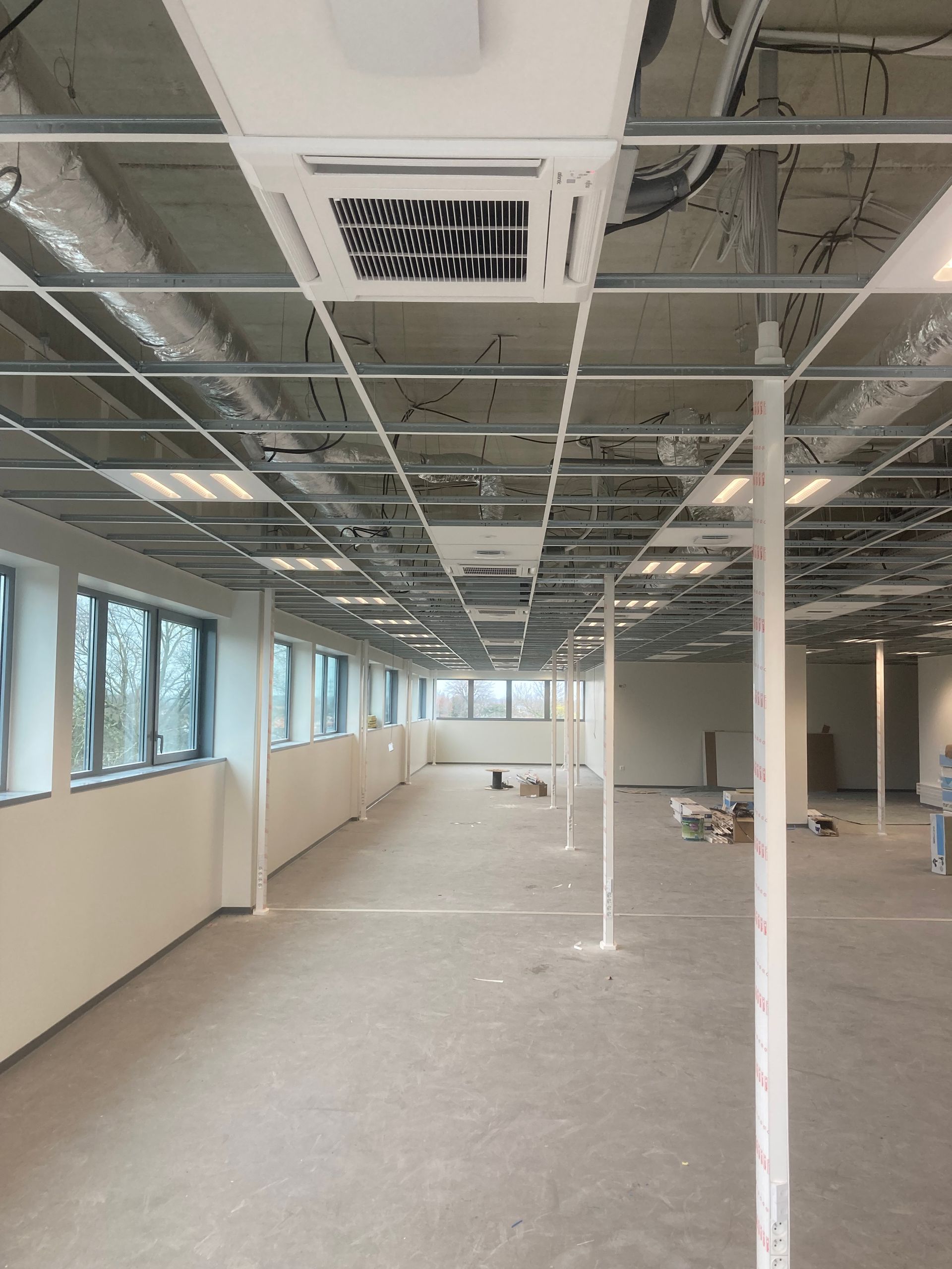 Espace de bureau vide avec grille de plafond apparente, système de chauffage, ventilation et climatisation.