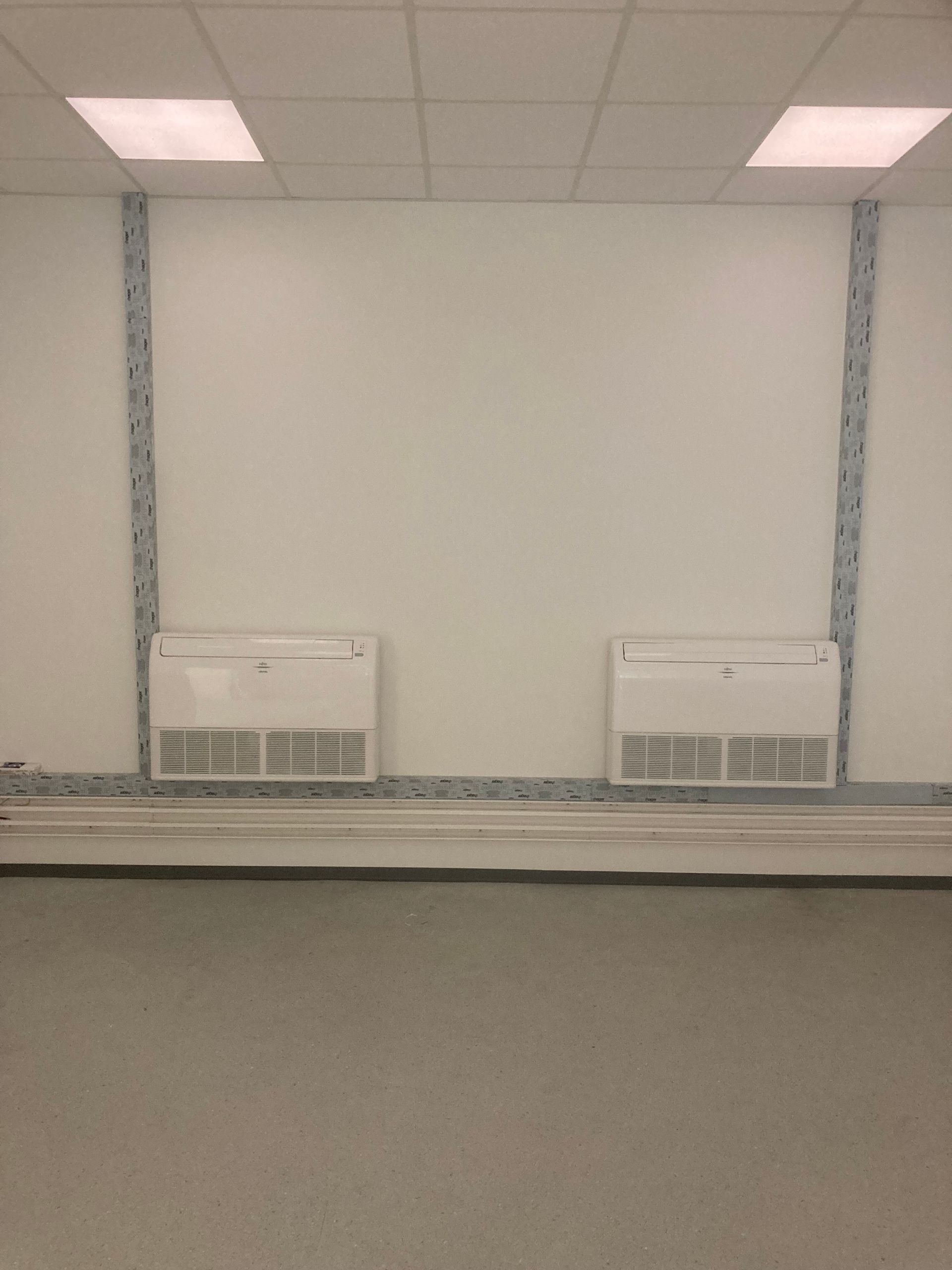 Mur blanc avec deux unités de climatisation. Supports métalliques et plinthe métallique au sol.
