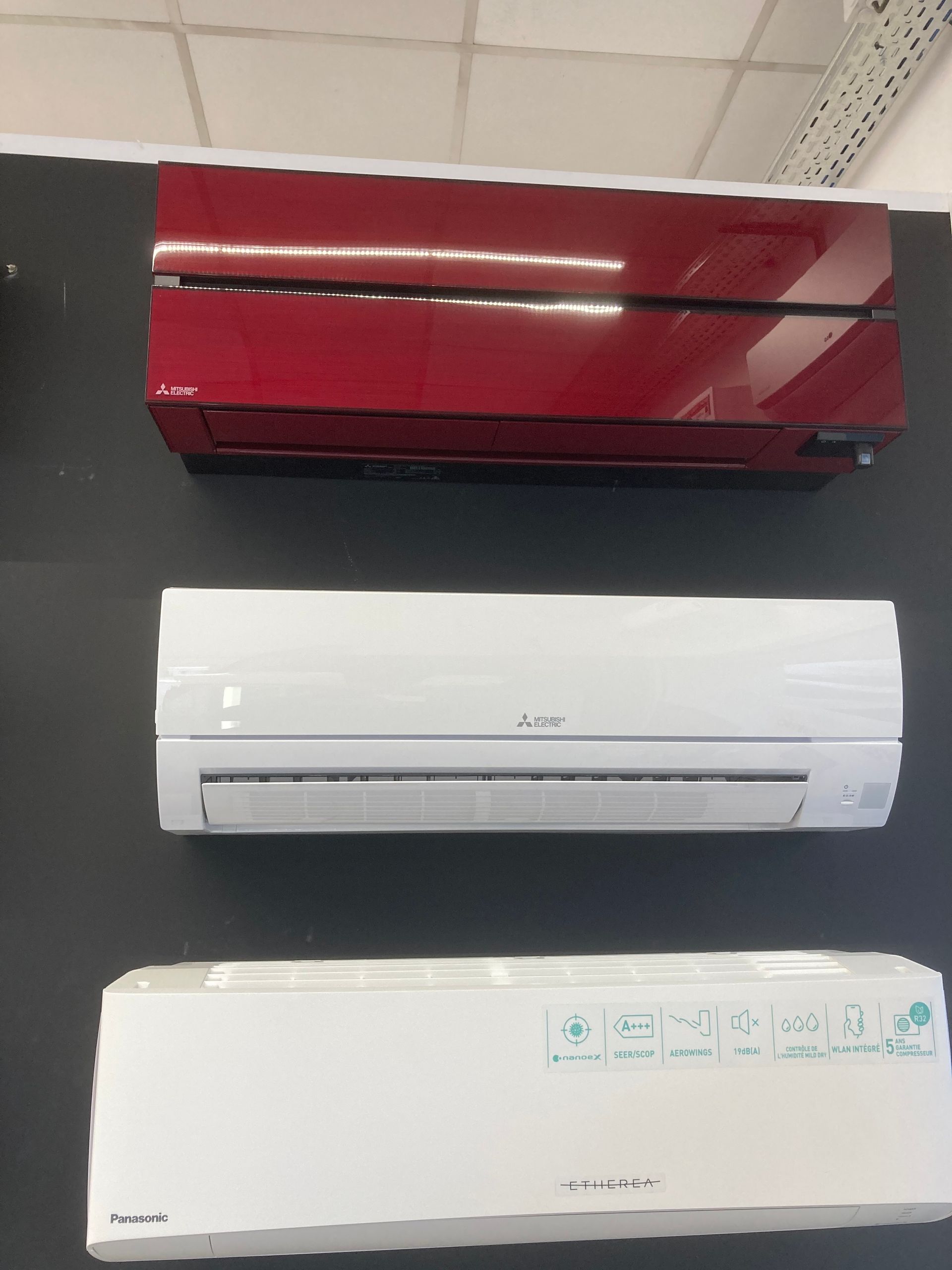 Trois unités de climatisation de couleurs différentes sont fixées sur un mur sombre.