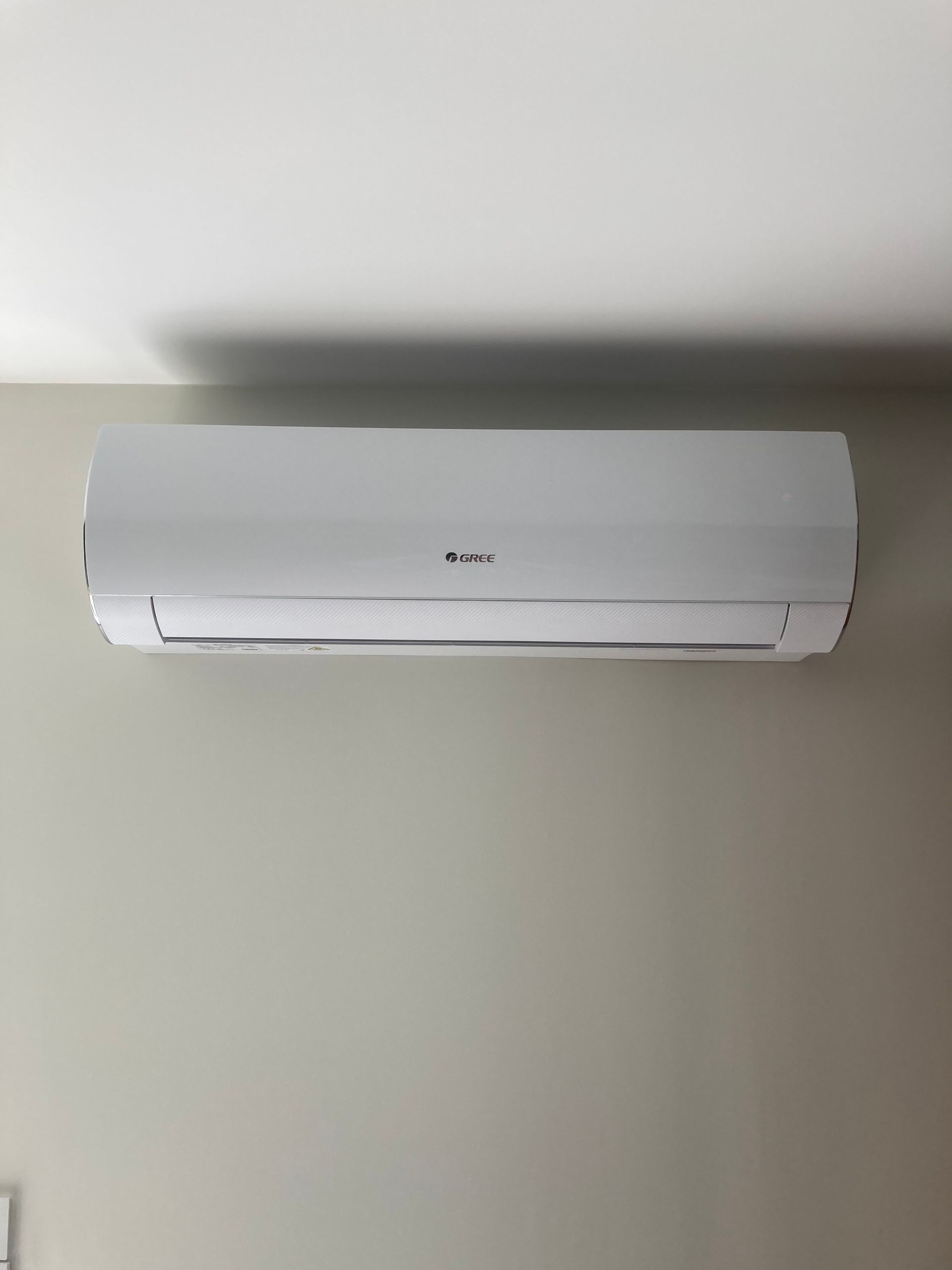 Climatiseur mural blanc sur un mur gris clair.