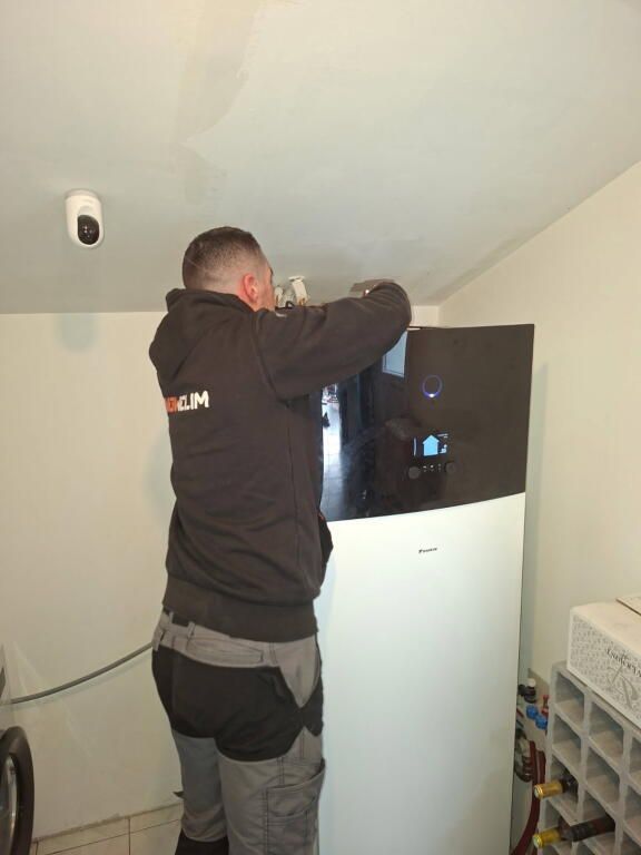 Un ouvrier soude près d'un climatiseur soulevé par des chaînes sur un toit.