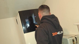 Trois ouvriers installent des unités de climatisation sur le toit d'un immeuble. Une grue soulève deux unités.