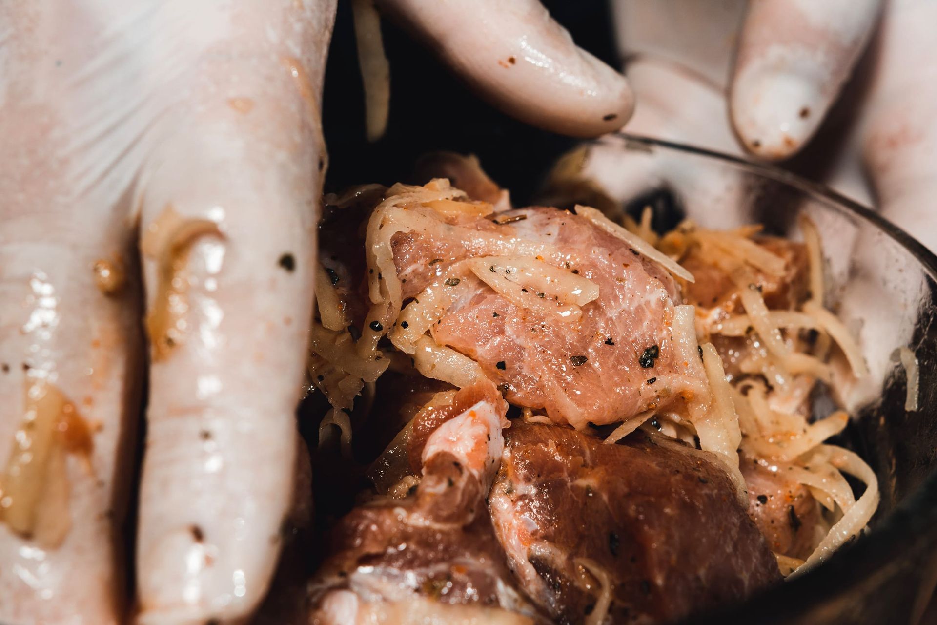 Manos enguantadas colocan pollo crudo sazonado con cebollas en rodajas en un tazón.