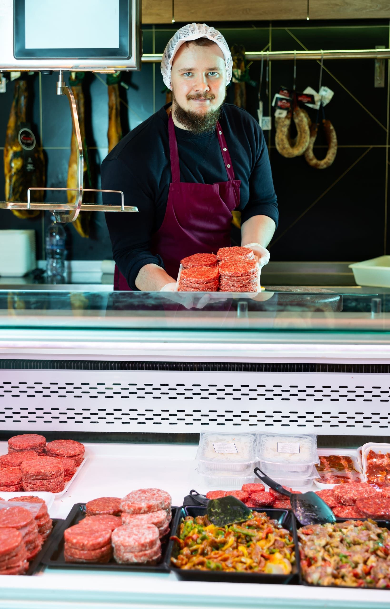 Carnicero detrás del mostrador de la charcutería, colocando la carne picada y las bandejas de comida preparada.
