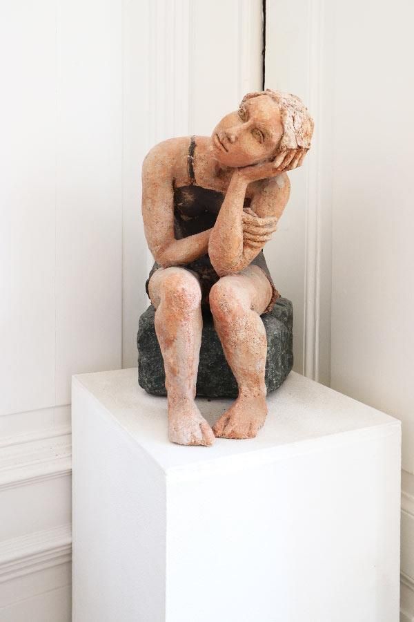 Eine Statue einer Frau, die auf einem weißen Würfel sitzt.