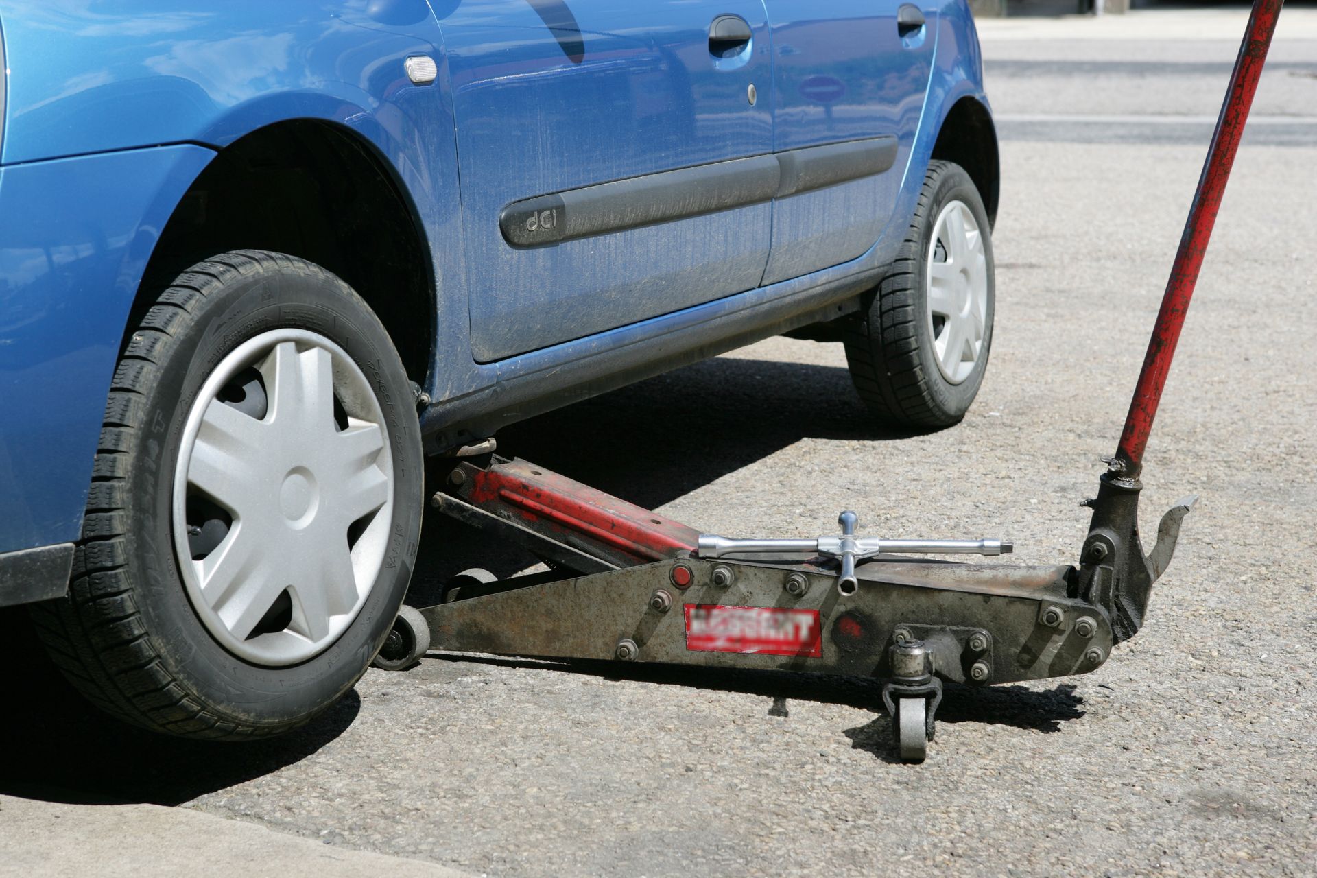 Voiture bleue soulevée par un cric hydraulique, prête pour un changement de pneu.