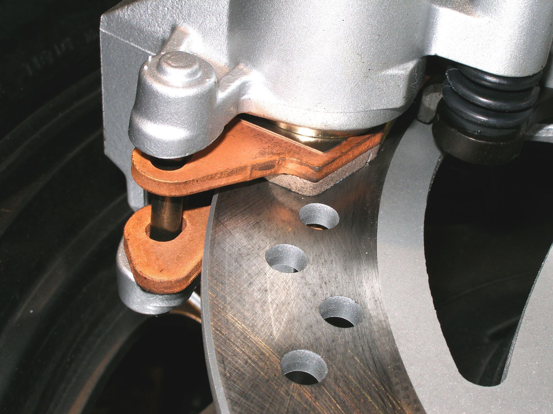 Gros plan sur un système de freinage automobile avec un étrier métallique, une plaquette de frein et un disque.