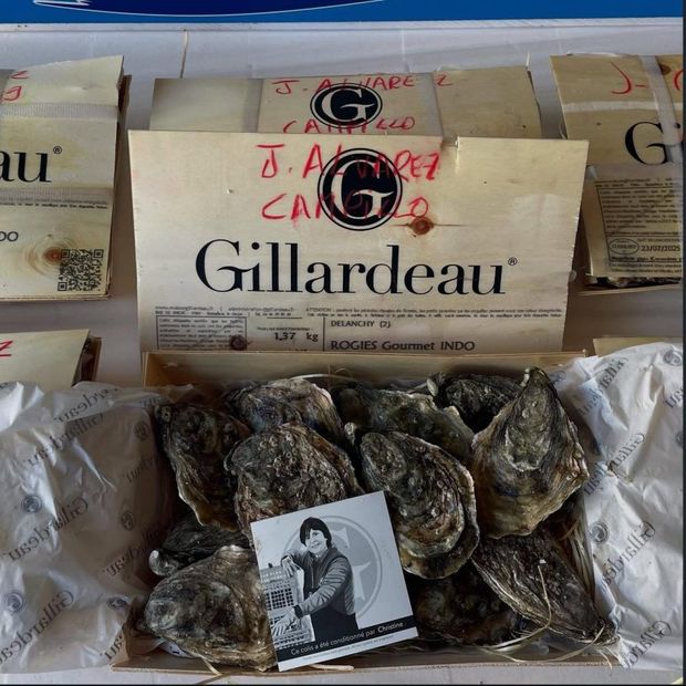 Una caja de madera con ostras Gillardeau, etiquetas escritas a mano y una pequeña tarjeta con un retrato sobre las conchas.