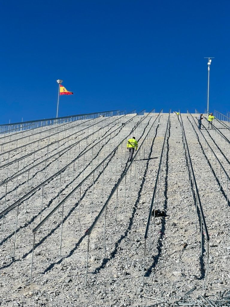 Trabajadores con chalecos amarillos en una ladera rocosa y empinada, con hileras de varillas metálicas