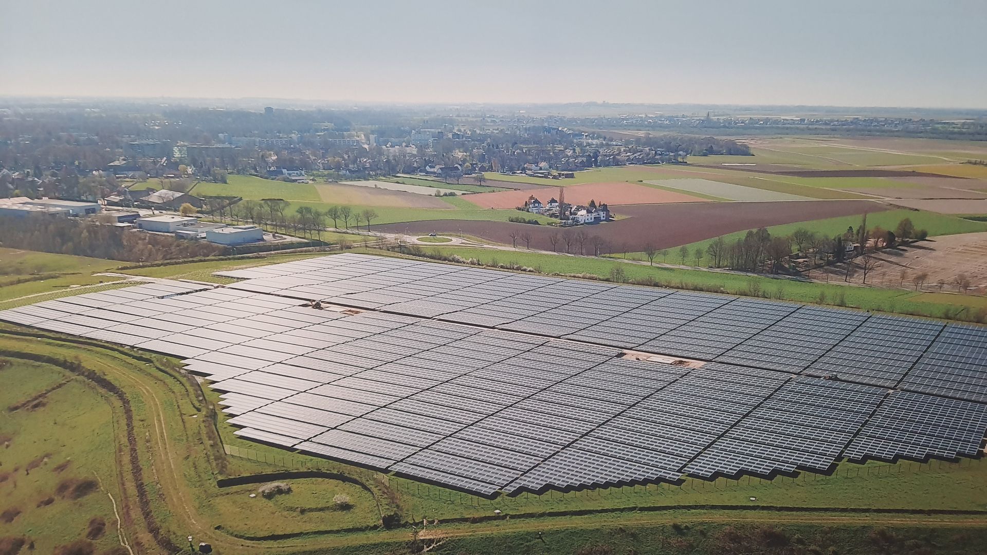 Vista aérea de una gran granja de paneles solares en un campo, con una ciudad al fondo.