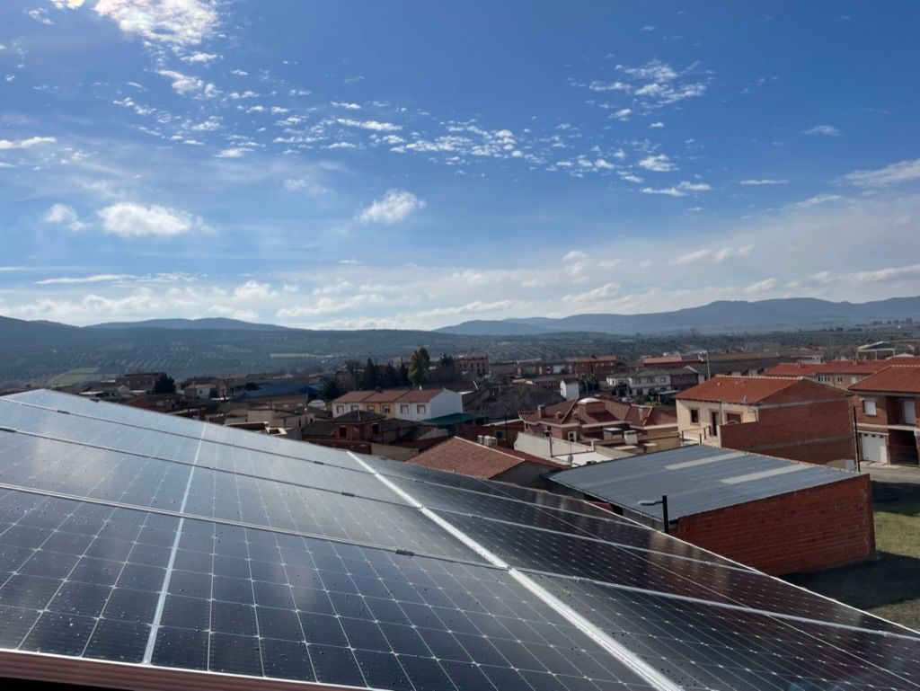 Paneles solares en un tejado con vistas a una ciudad con tejados de tejas rojas bajo un cielo azul con nubes.