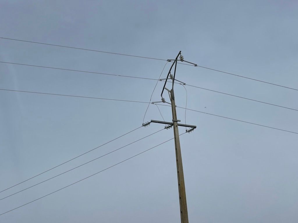 Cables eléctricos en un poste de madera contra un cielo pálido y nublado.