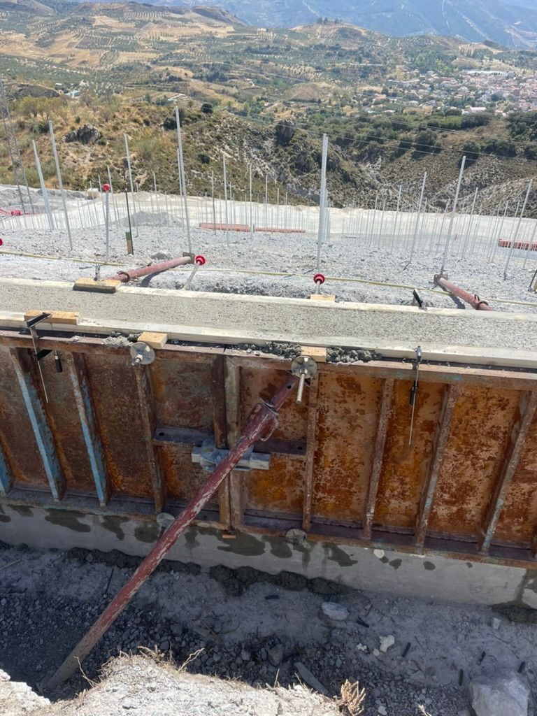 Sitio de construcción con encofrado metálico que sostiene el hormigón, ladera al fondo.