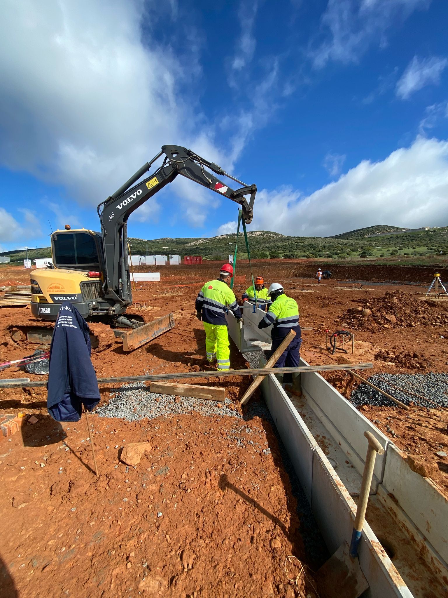 Trabajadores de la construcción con chalecos de seguridad y una retroexcavadora en un sitio de construcción