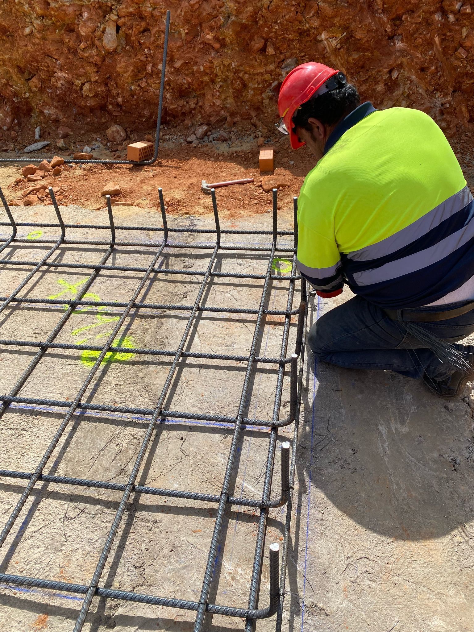 Obrero de la construcción doblando una rejilla de varillas de refuerzo sobre hormigón, vistiendo un casco de seguridad