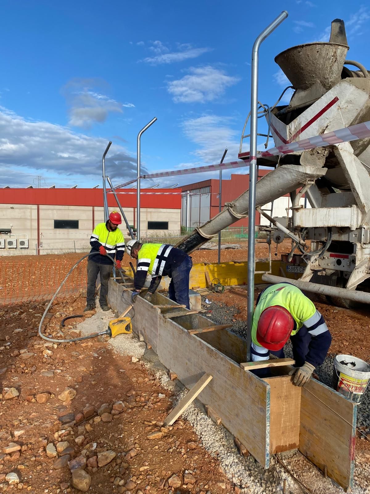 Obreros de la construcción vierten hormigón desde un camión en encofrados de madera al aire libre.