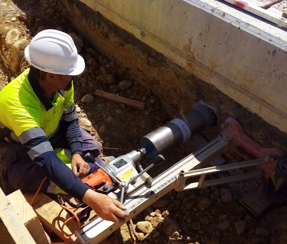 Trabajador de la construcción que utiliza un taladro para perforar un agujero en el hormigón cerca de unos cimientos.