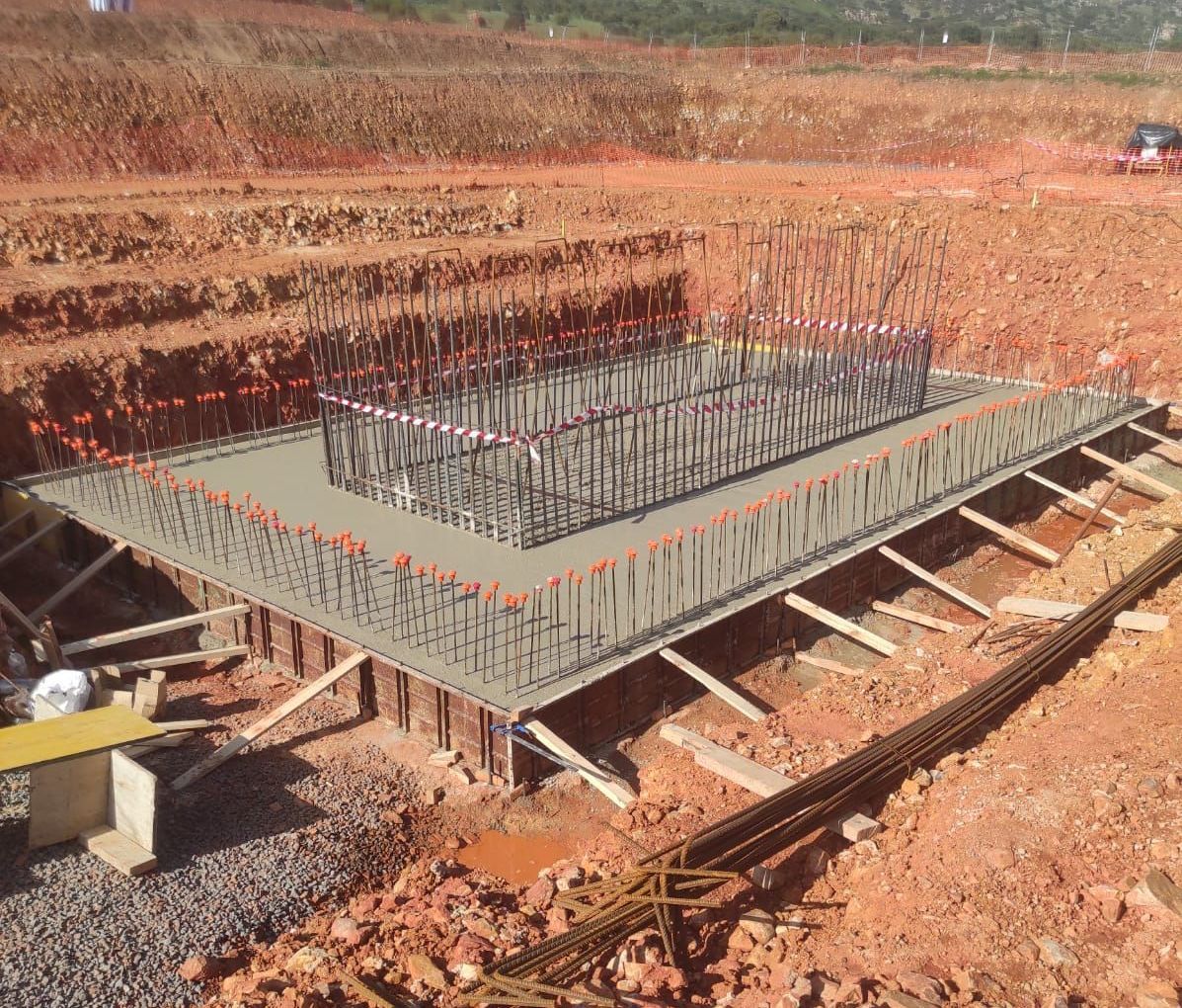Obra con cimentación de hormigón y estructura de varillas corrugadas. Soportes de madera sobre tierra marrón rojiza.