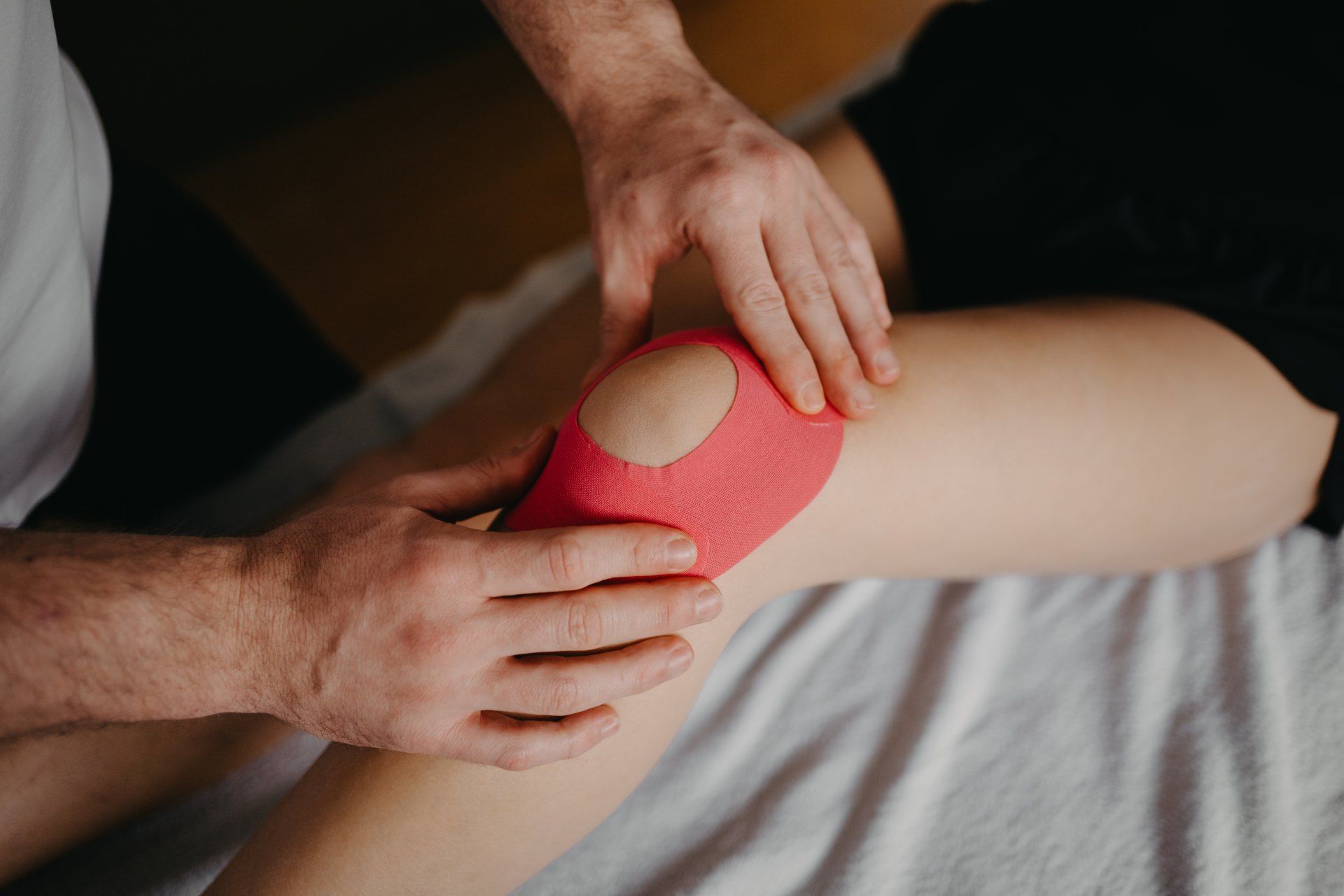Knie mit rosa Kinesiologie-Tape; das Tape wird von Hand angelegt.
