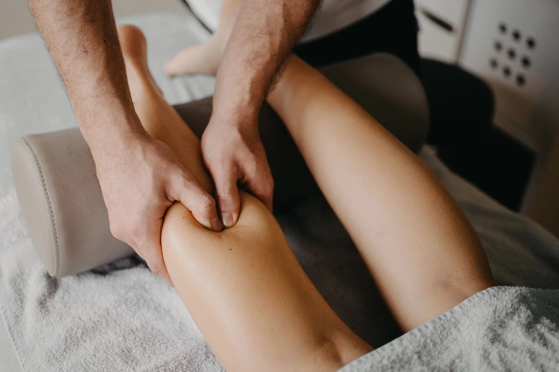 Hände massieren das Bein einer Person in einem Spa oder einer Klinik; das Bein ruht auf einer gepolsterten Liege.