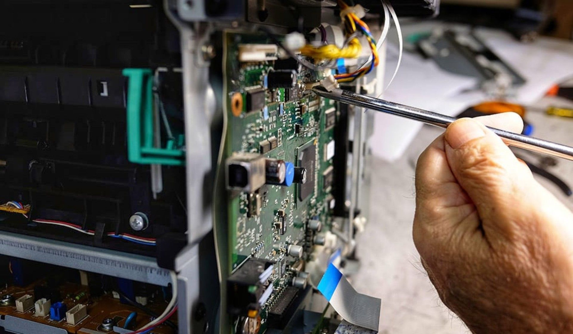 Eine Hand benutzt einen Schraubendreher, um eine elektronische Leiterplatte im Inneren einer Maschine zu reparieren.