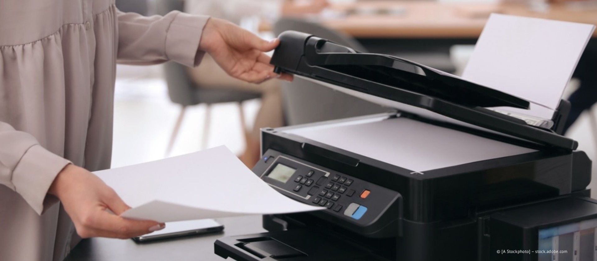 Eine Person legt Papier in einen schwarzen Bürodrucker-Scanner auf einem Schreibtisch ein.