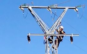 Un hombre está trabajando en una línea eléctrica con un cielo azul de fondo.