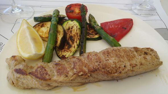 Un plato blanco cubierto con un trozo de carne y verduras.