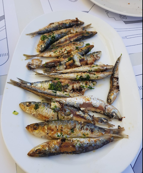 Un plato blanco cubierto con sardinas fritas sobre una mesa.