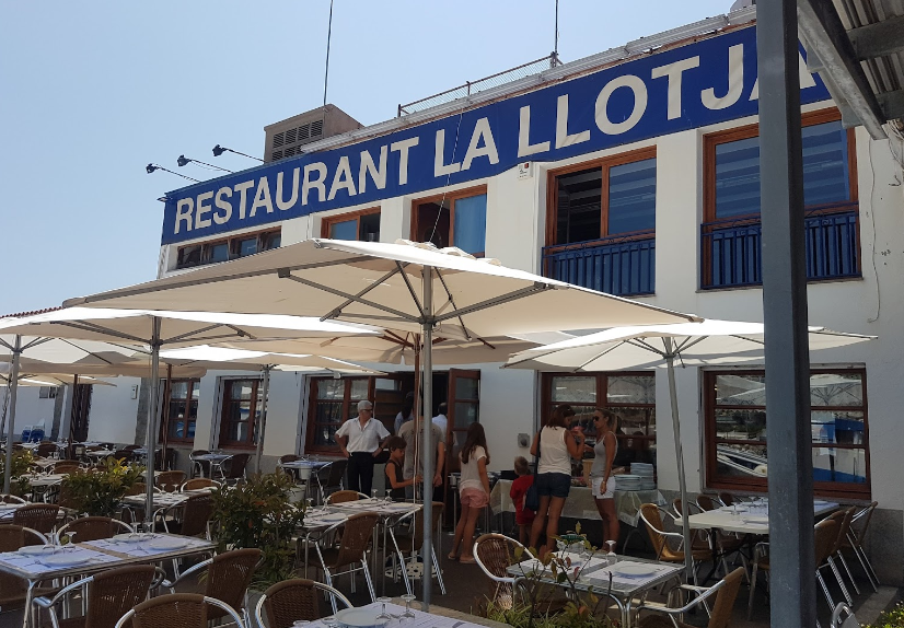 Un restaurante con mesas y sombrillas delante.