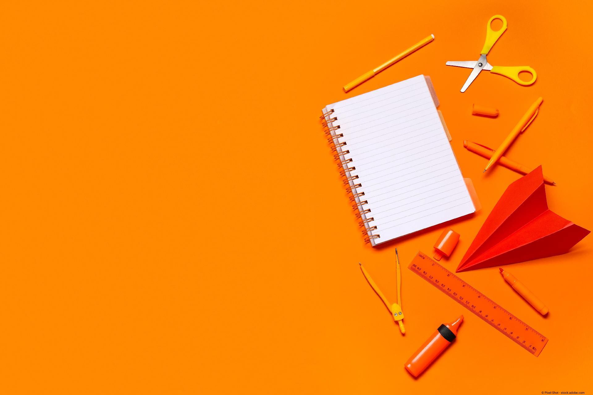 Verschiedene Schreibwaren liegen auf einem orangefarbenen Hintergrund