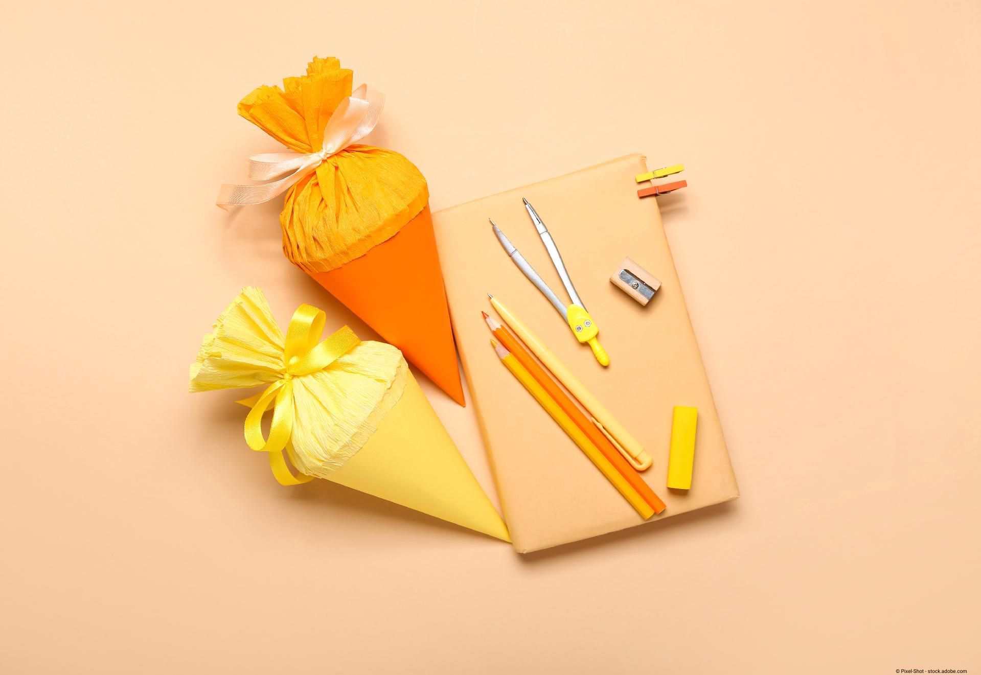 Zwei Schultüten liegen neben Schreibwaren auf einem pastellfarbenen Hintergrund