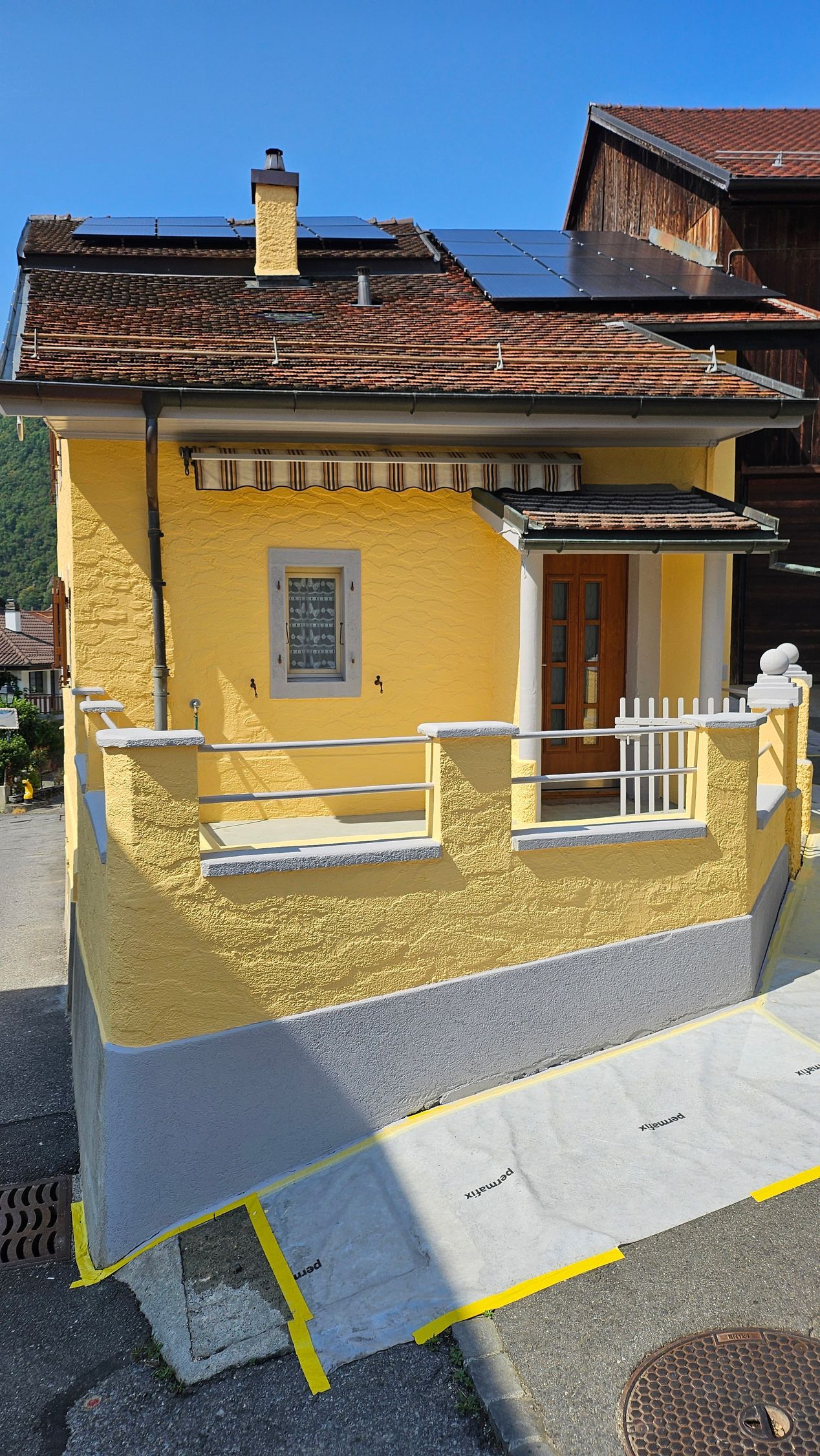 Échafaudage près d'un bâtiment moderne, avec un escabeau appuyé contre celui-ci. Arbres verts et ciel bleu.