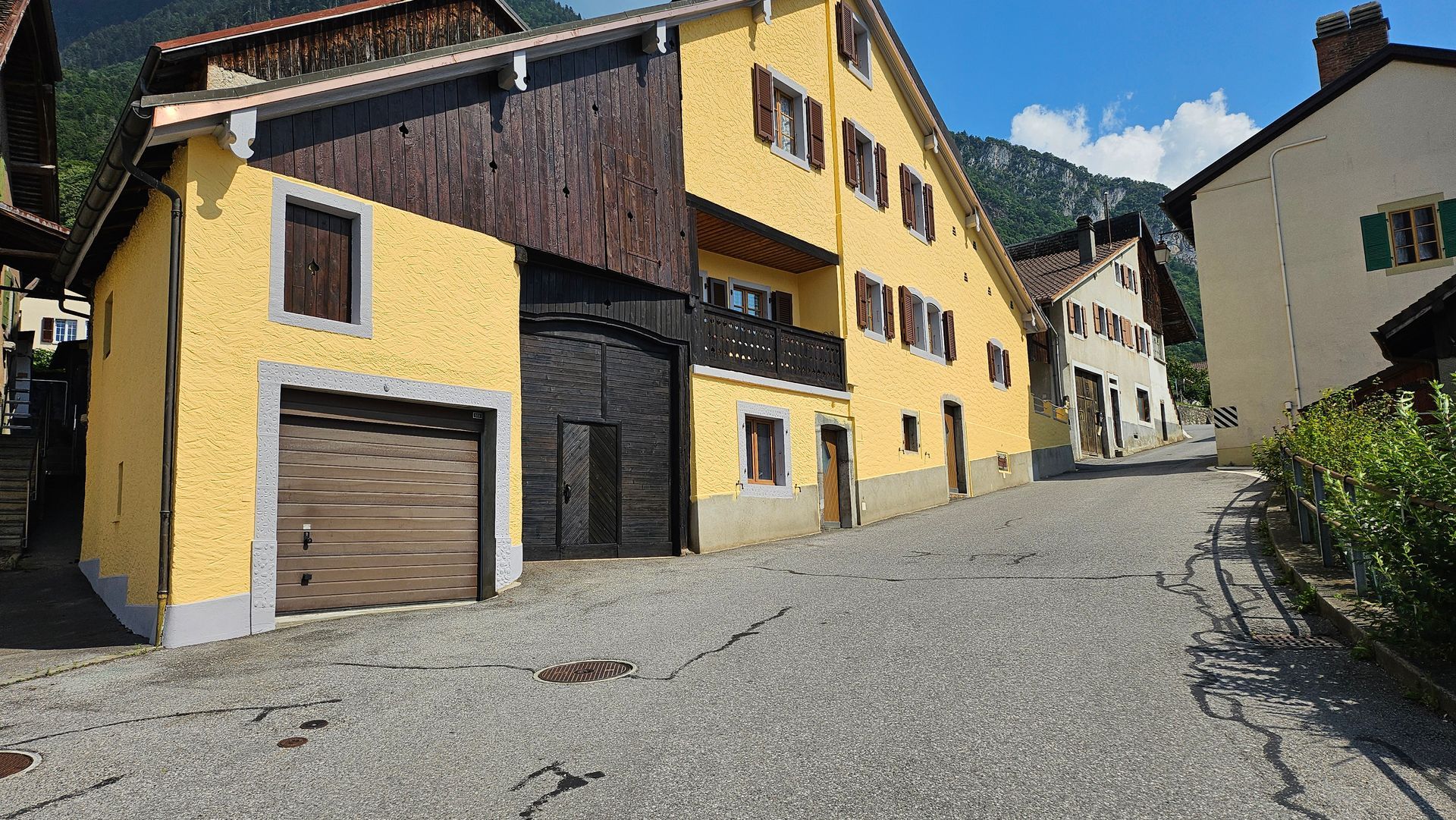 Une clôture en fer forgé noir surmonte un mur de pierre, avec une clôture blanche et des montagnes en arrière-plan.