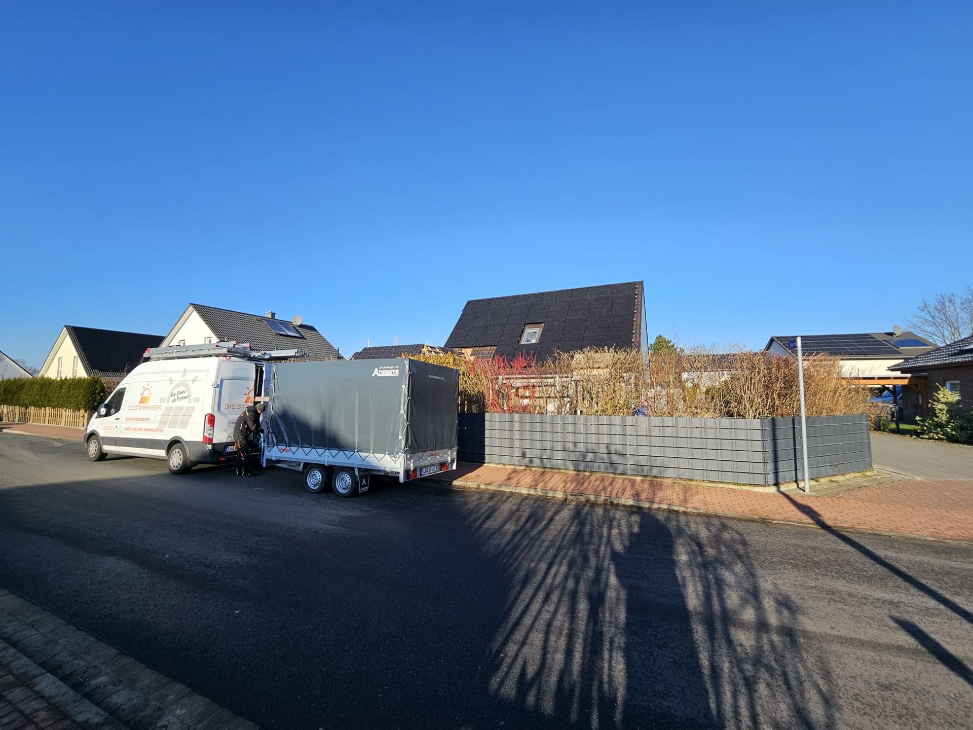 Ein weißer Lieferwagen zieht einen Anhänger eine Straße entlang.