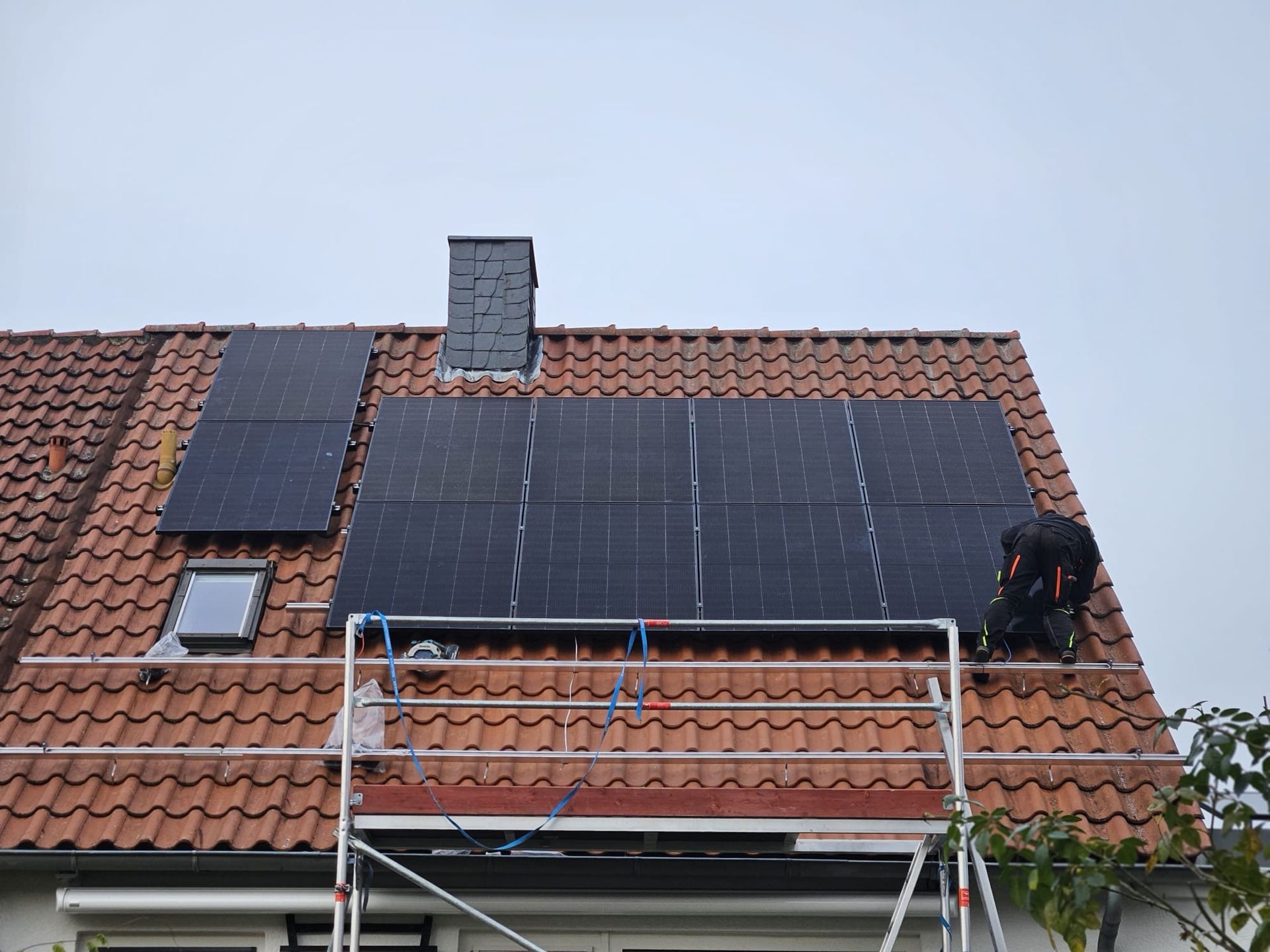 Ein Mann installiert Solarmodule auf dem Dach eines Hauses.