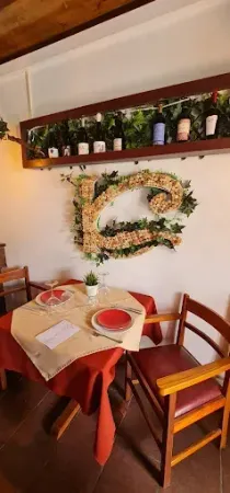 Mesa de restaurante puesta para dos, con platos rojos, una pequeña planta y una gran letra