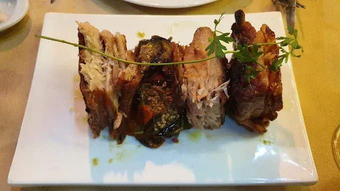 Un plato blanco rectangular con carnes asadas: cerdo y un plato de verduras, adornado con hierbas.