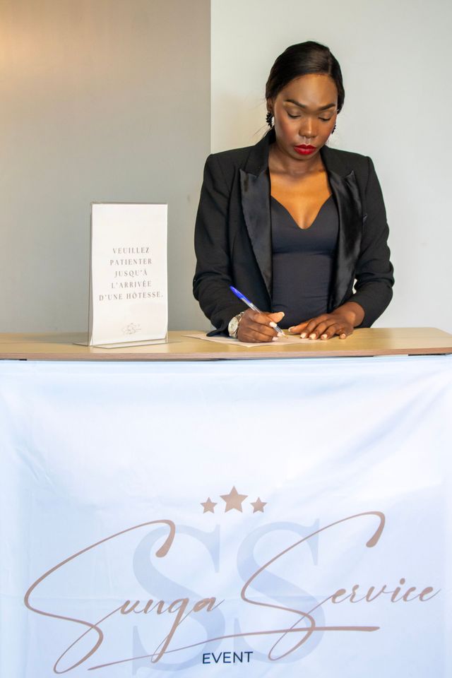 Une femme signe des documents à une table d'inscription avec le logo « Sunga Service Event ».