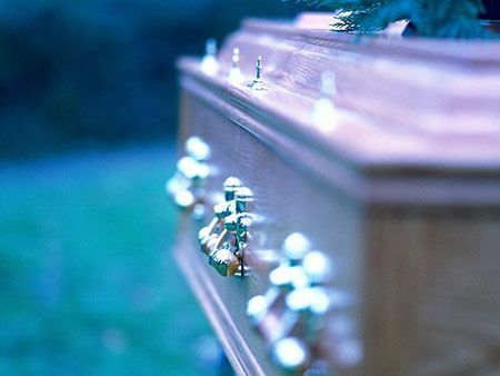 Cercueil en bois avec poignées en laiton, à l'extérieur ; fond bleu-vert.