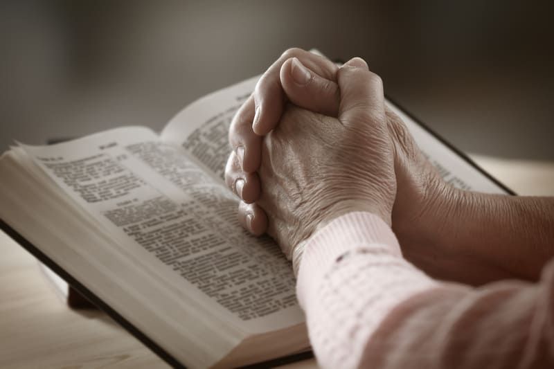 Eine Frau betet mit ihren Händen auf einem offenen Buch | St. Brigida Seniorenzentrum