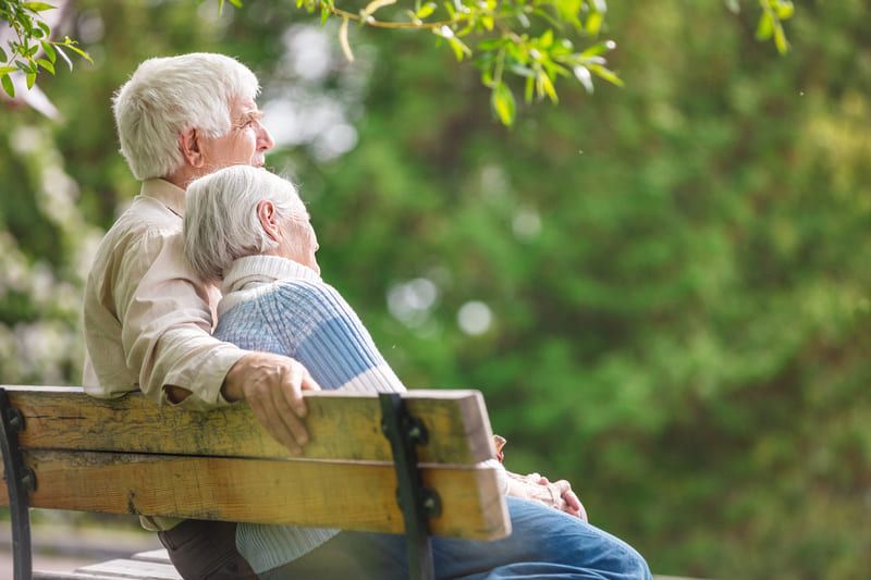 Ein älteres Paar sitzt auf einer Parkbank und umarmt sich | St. Brigida Seniorenzentrum
