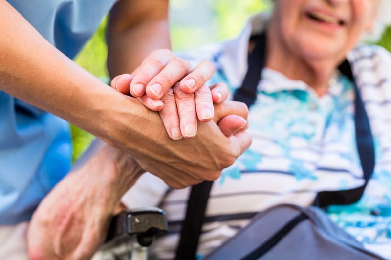 Eine Krankenschwester hält die Hand einer älteren Frau in einem Rollstuhl | St. Brigida Seniorenzentrum