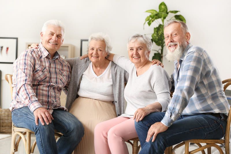 Eine Gruppe von älteren Menschen sitzt auf Stühlen und lächelt in die Kamera | St. Brigida Seniorenzentrum