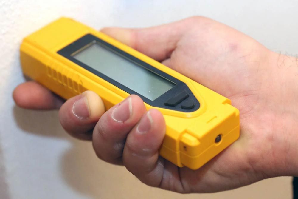 Eine Hand hält einen gelben Balkensucher an eine weiße Wand.