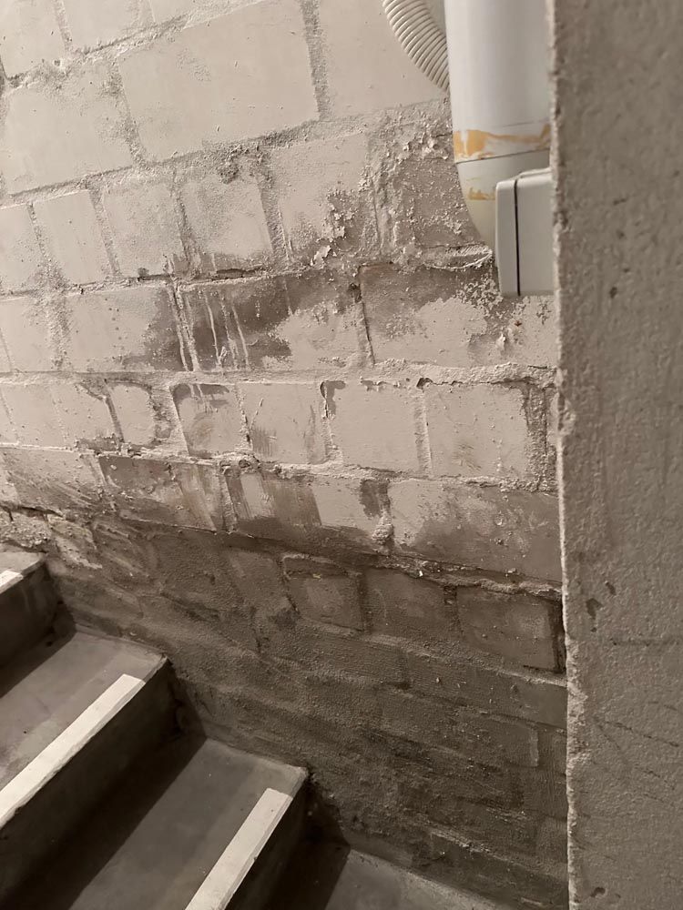 Eine Betonblockwand mit Wasserschaden an einem Treppenaufgang in einem Gebäude.