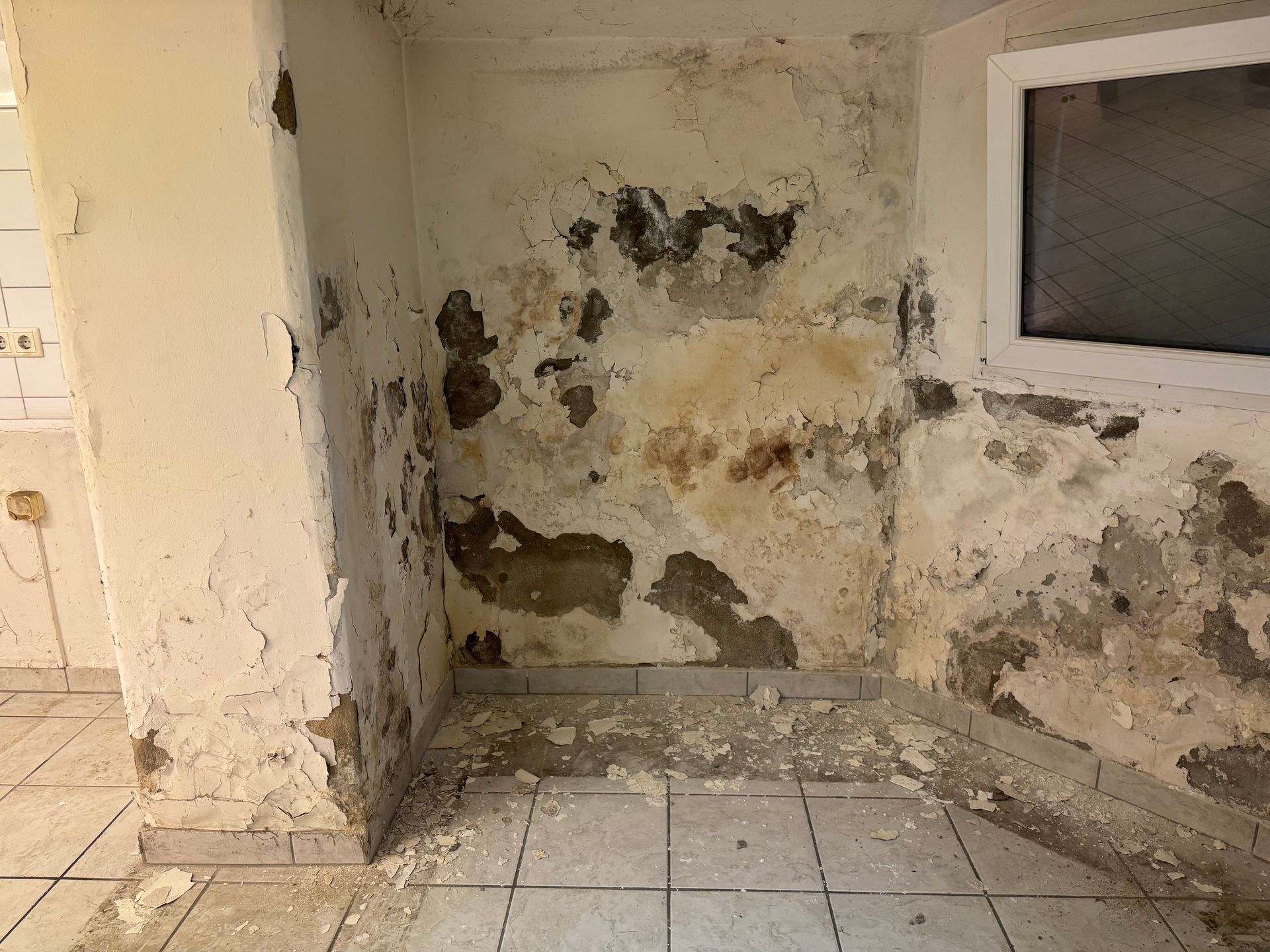 Beschädigte Innenwandecke mit abblätternder Farbe und sichtbaren Wasserschäden in der Nähe eines Fensters.